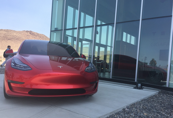 Der Model 3 Prototyp. Im Hintergrund: Teslas Gigafactory. Bildquelle: The Motley Fool.