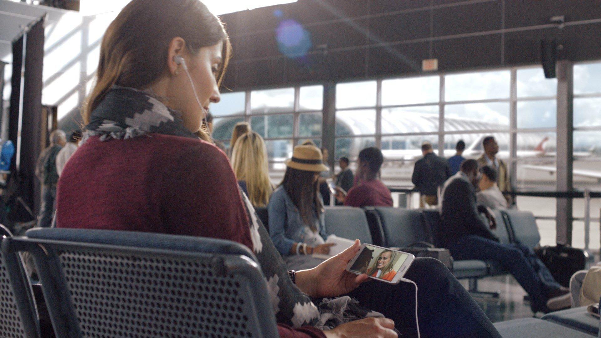 Frau sieht sich am Flughafen Netflix am Handy an (Netflix Aktie)