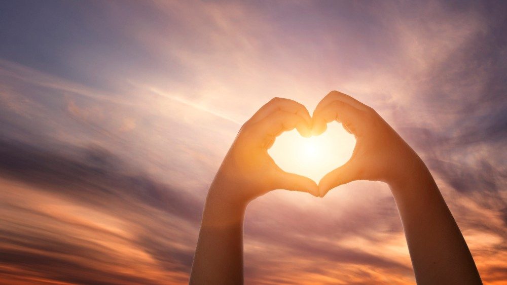 Close up of child hands forming heart shape over beautiful sky