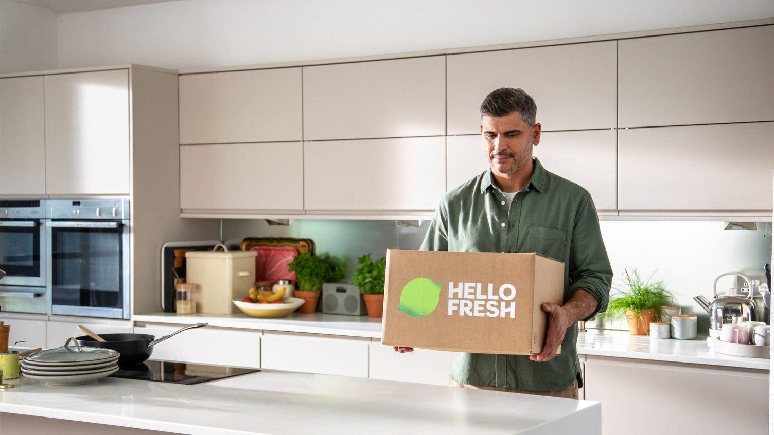 Ein Mann in einer Küche hält eine HelloFresh-Box mit Nahrungsmitteln