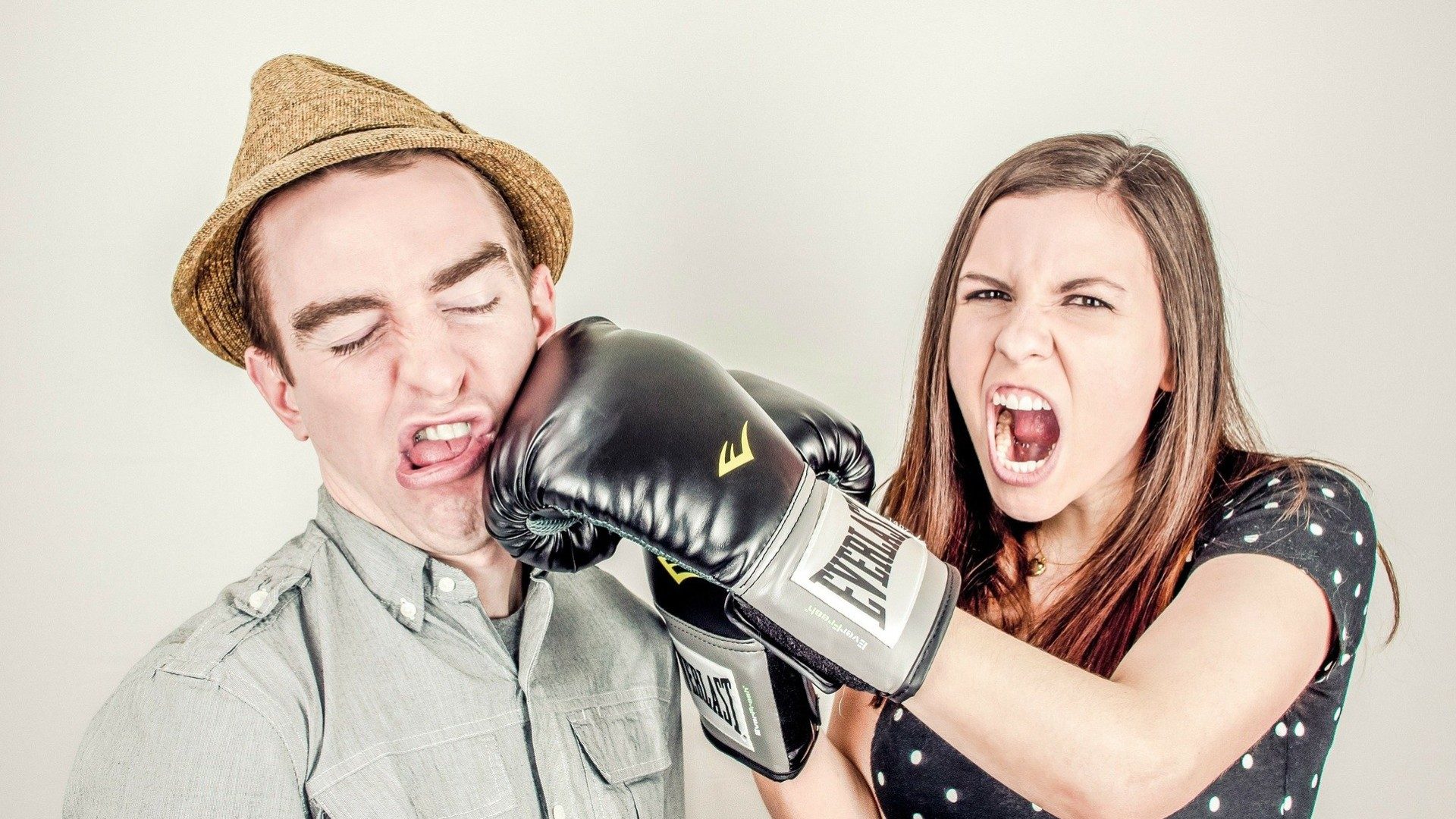 Eine Frau schlägt einen Mann mit einem Boxhandschuh ins Gesicht. Die Frau brüllt dabei.