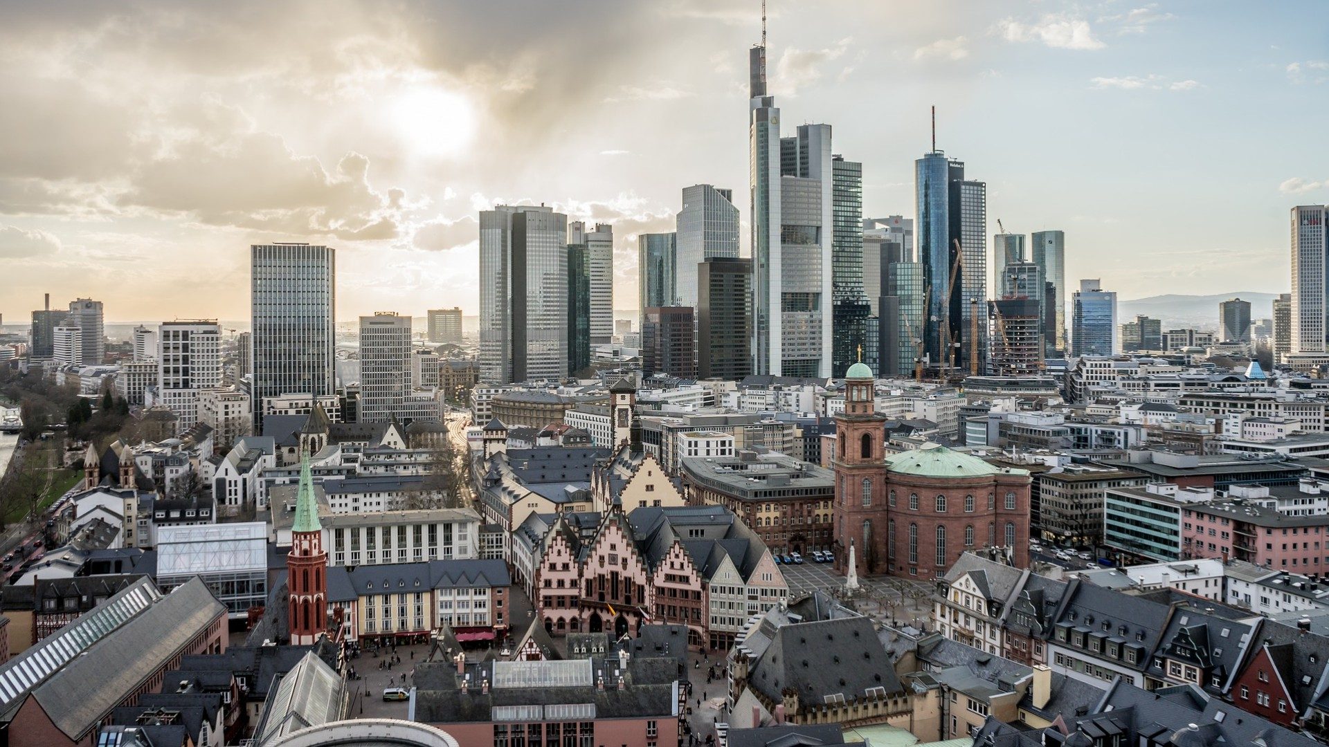 Skyline von Frankfurt am Main mit Sonne und kleinen Wolken im Hintergrund.