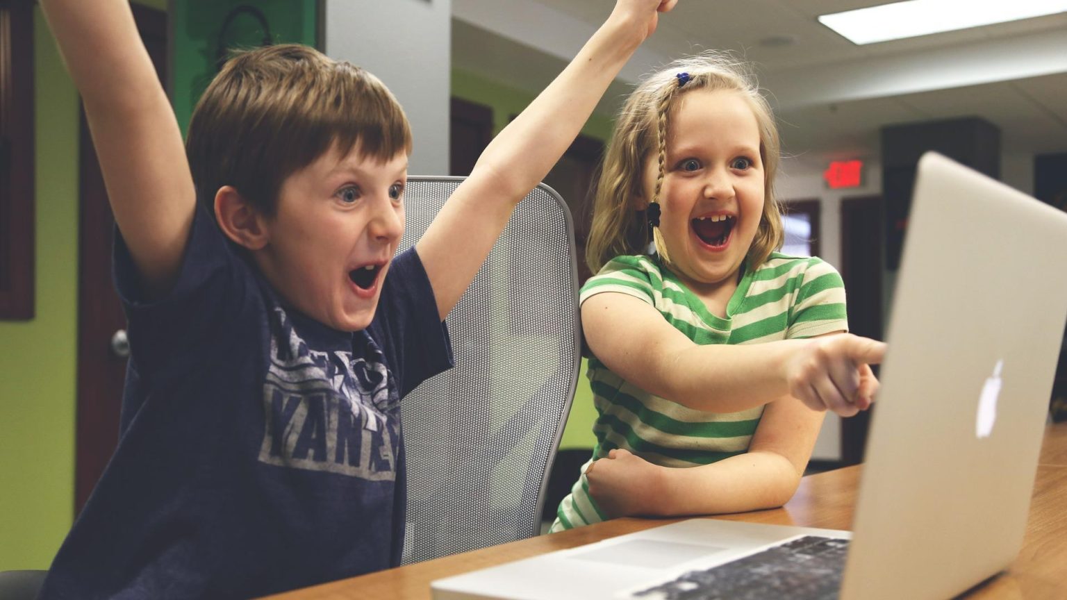 zwei Kinder sitzen jubelnd vor einem Apple MacBook