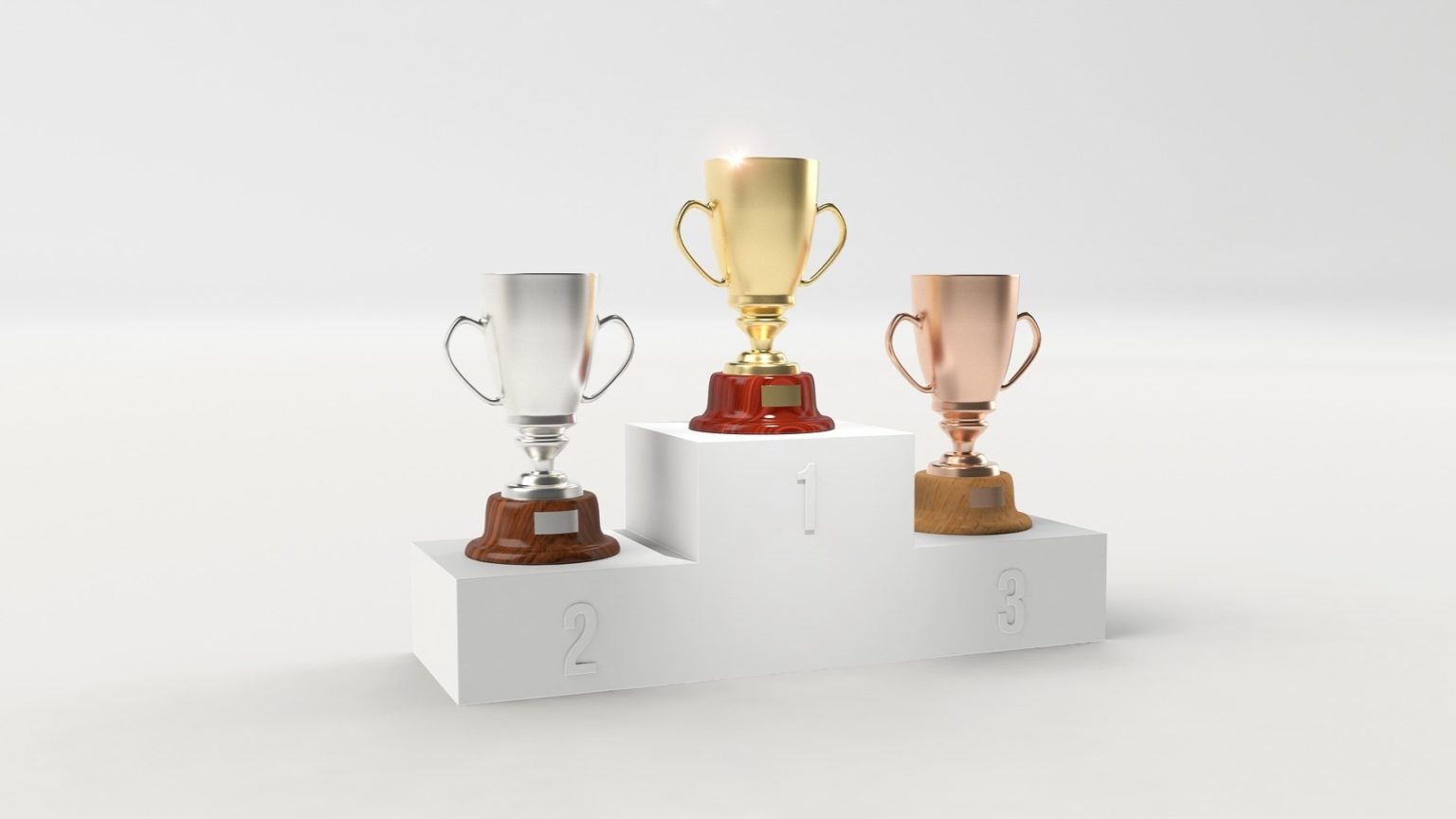 Auf einem Siegerpodest stehen ein Bronze- ein Silber- und ein Goldpokal