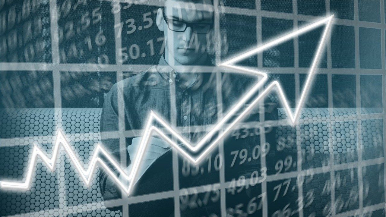 Ein Mann analysiert Finanzberichte, im Vordergrund Kursdaten und ein aufwärts zeigender Aktienchart