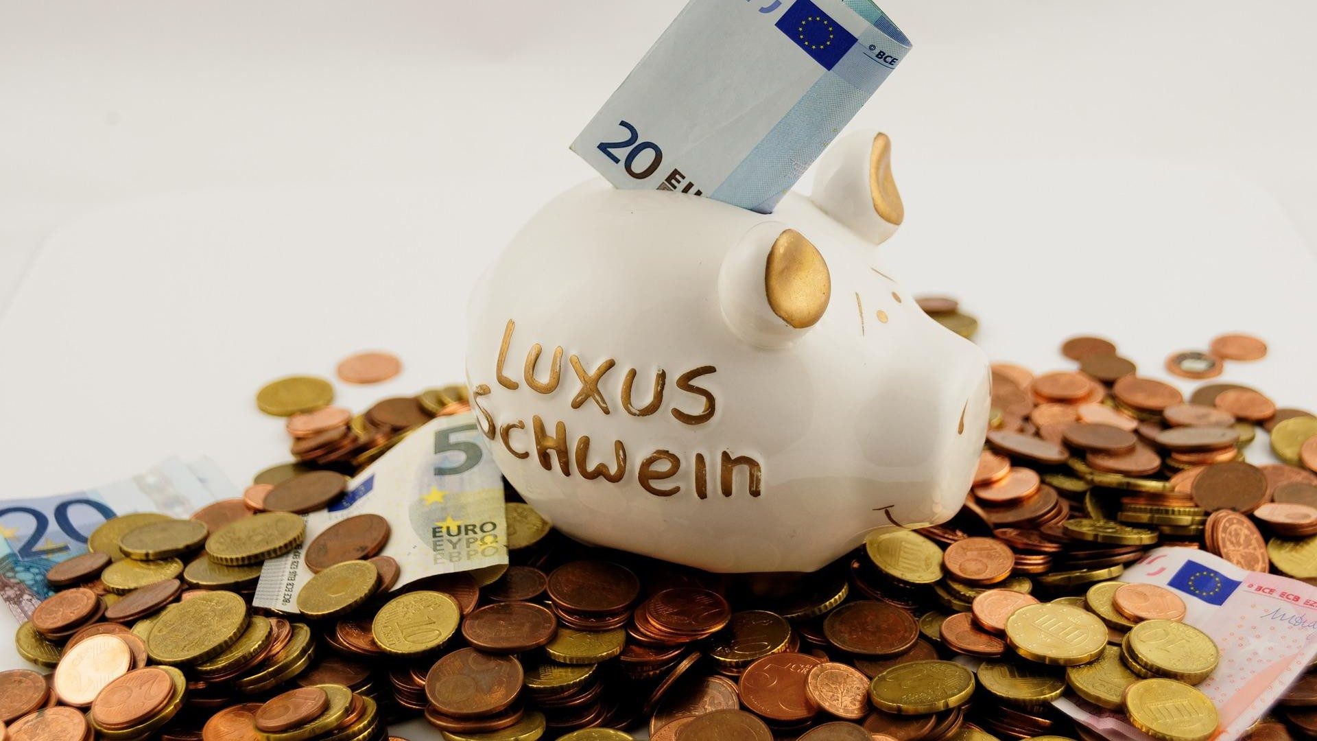 Ein von Münzen und Geldscheinen umgebenes Sparschwein wird mit 20 Euro gefüttert