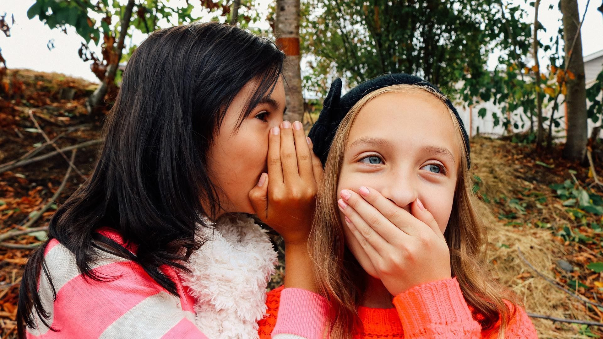 Zwei Mädchen flüstern sich ein Geheimnis ins Ohr.