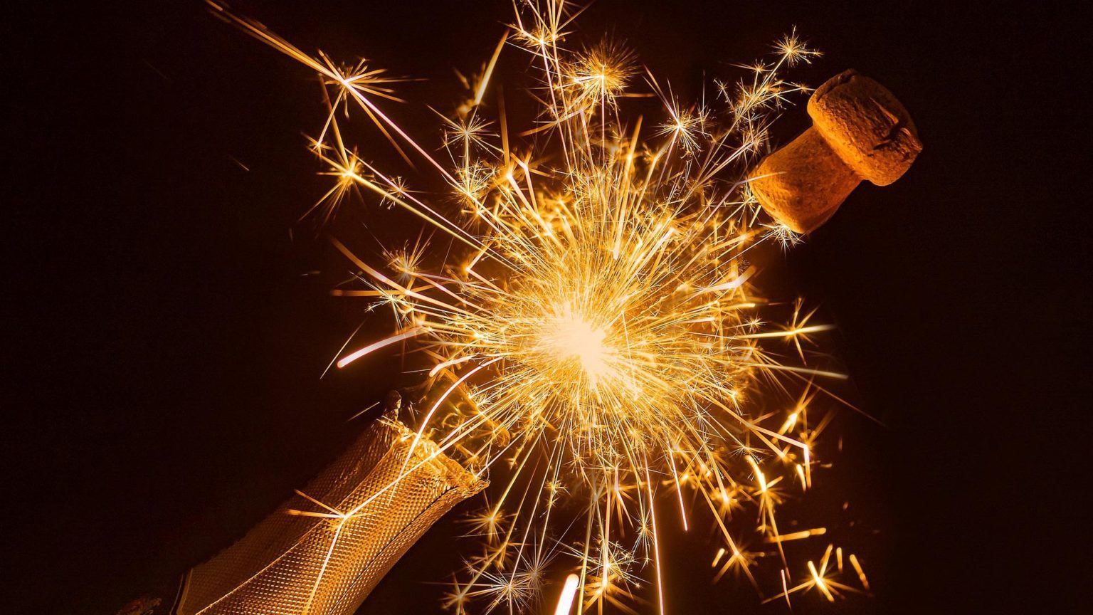 Eine Sektflasche aus der gerade der Korken mit einem Feuerwerk fliegt.