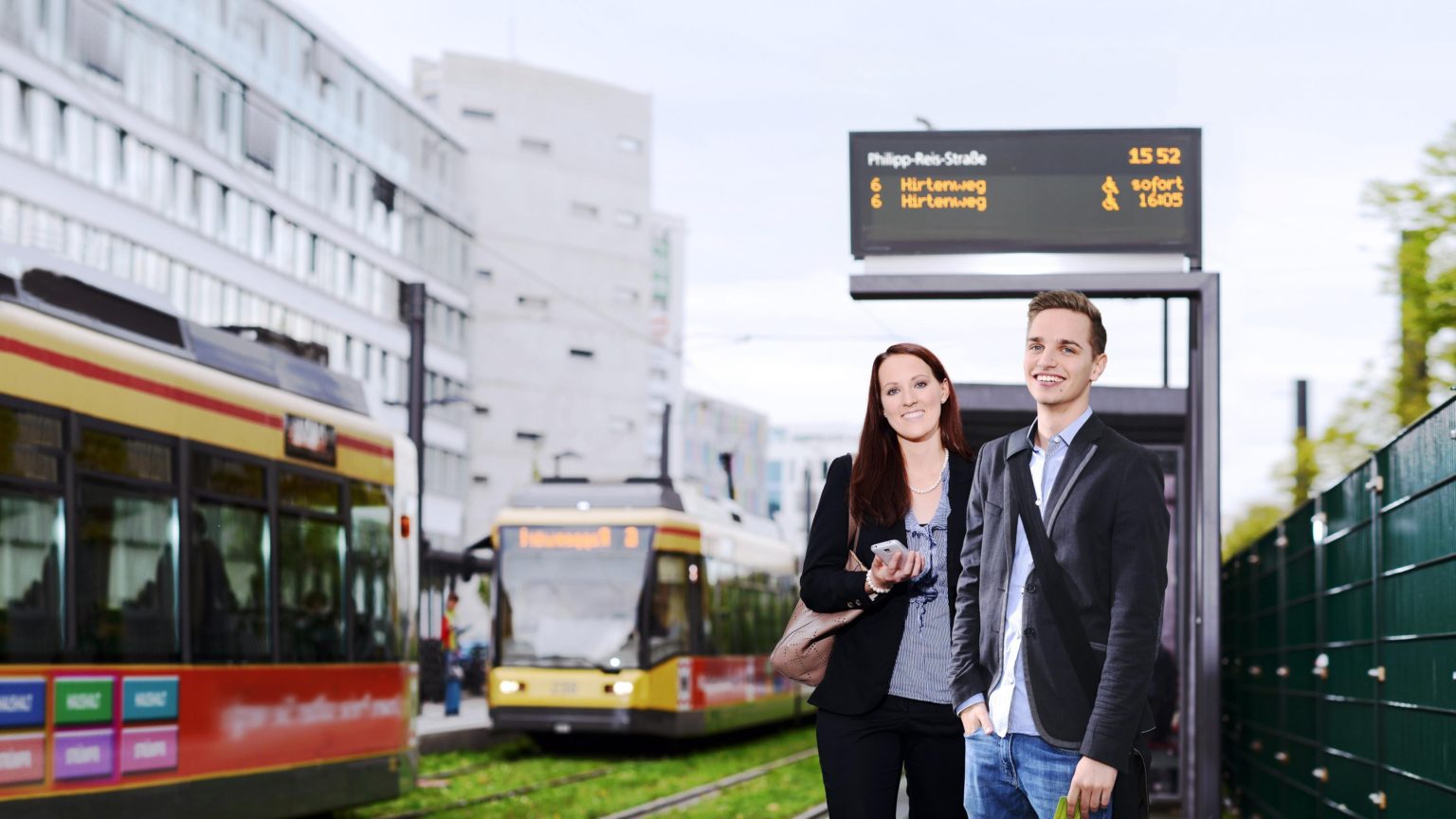 Fahrgäste warten auf ihr öffentliches Verkehrsmittel, Fahrgastinformation von init im Hintergrund