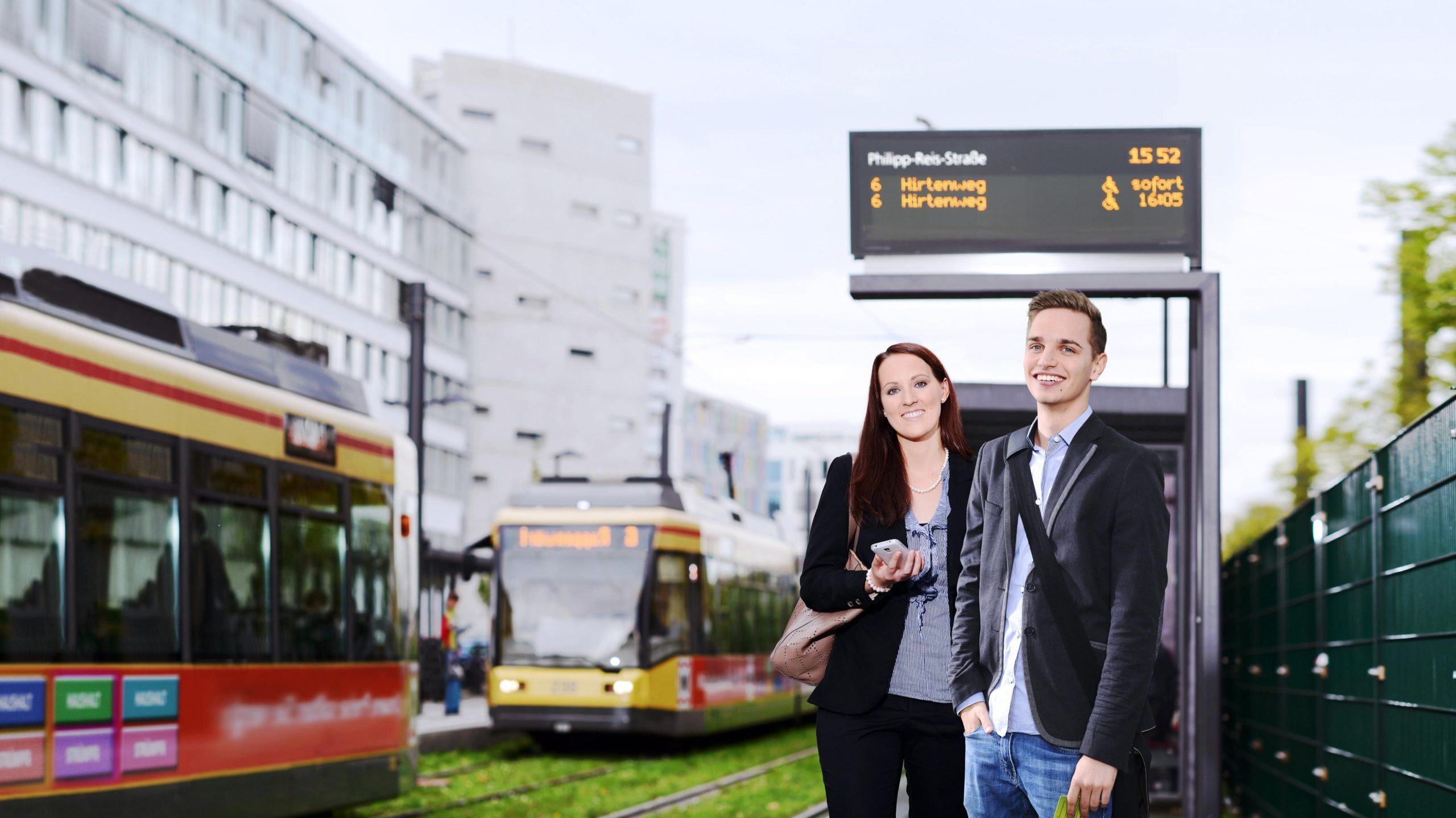 Fahrgäste warten auf ihr öffentliches Verkehrsmittel, Fahrgastinformation von init im Hintergrund
