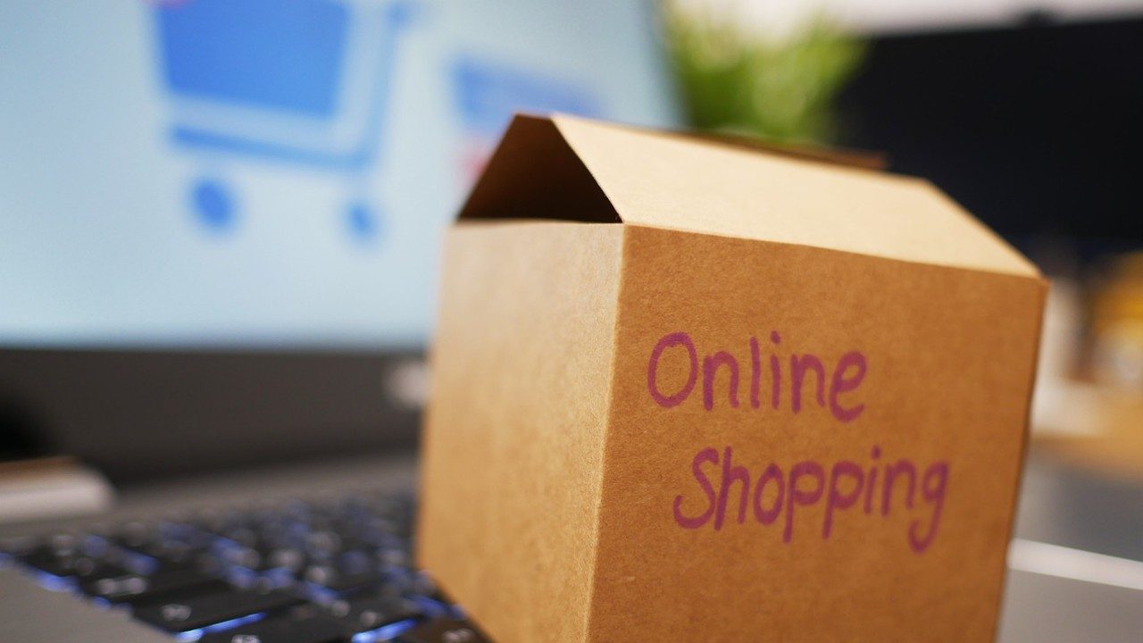 Auf der Tastatur eines Laptops liegt ein Paket mit Aufdruck Online Shopping.