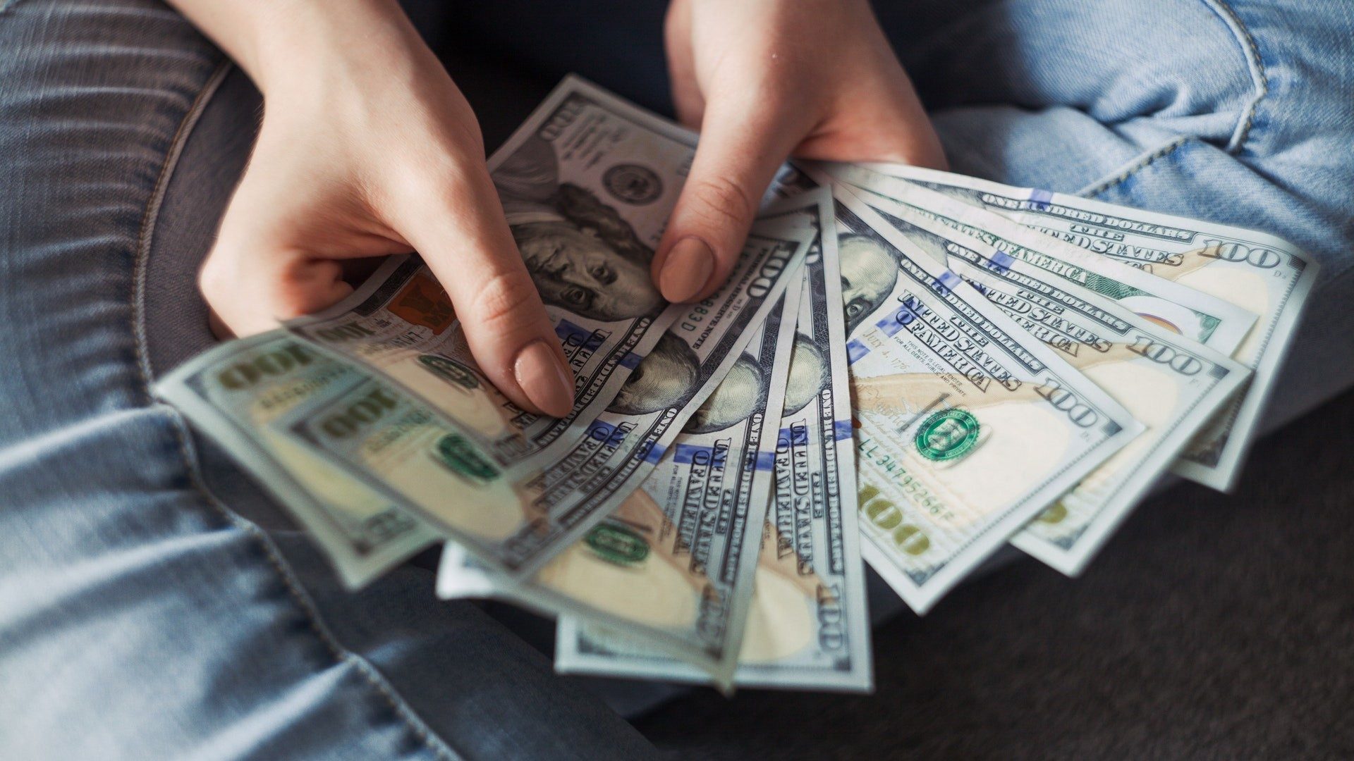 Eine Person hält 100-Dollar-Geldscheine aufgefächert in den Händen