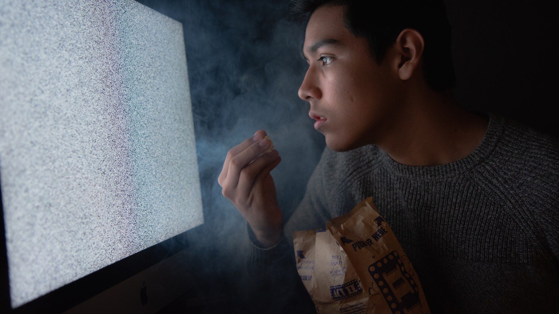 Ein Mann sitzt gebannt mit Snacks vor einem rauschenden Fernseher