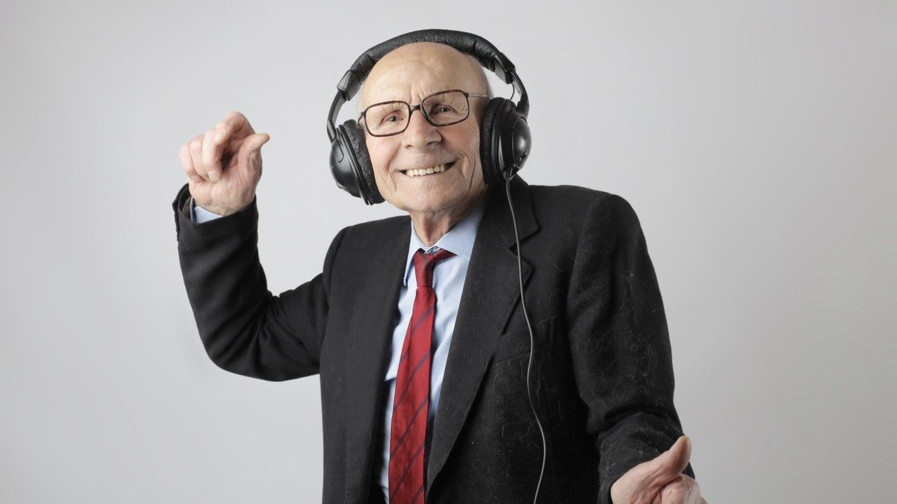 Ein freudiger alter Mann im Anzug tanzt zu Musik über Kopfhörer