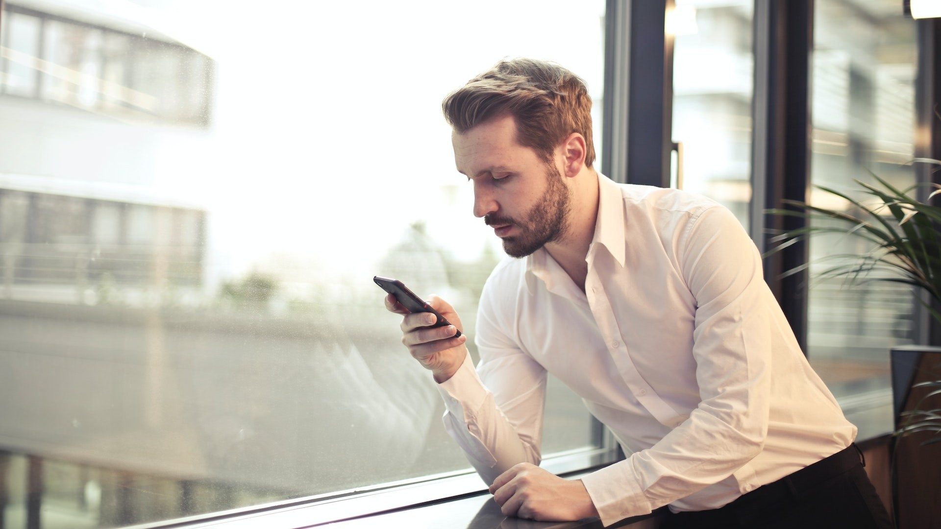 Ein Geschäftsmann im weißen Hemd schaut auf sein Smartphone