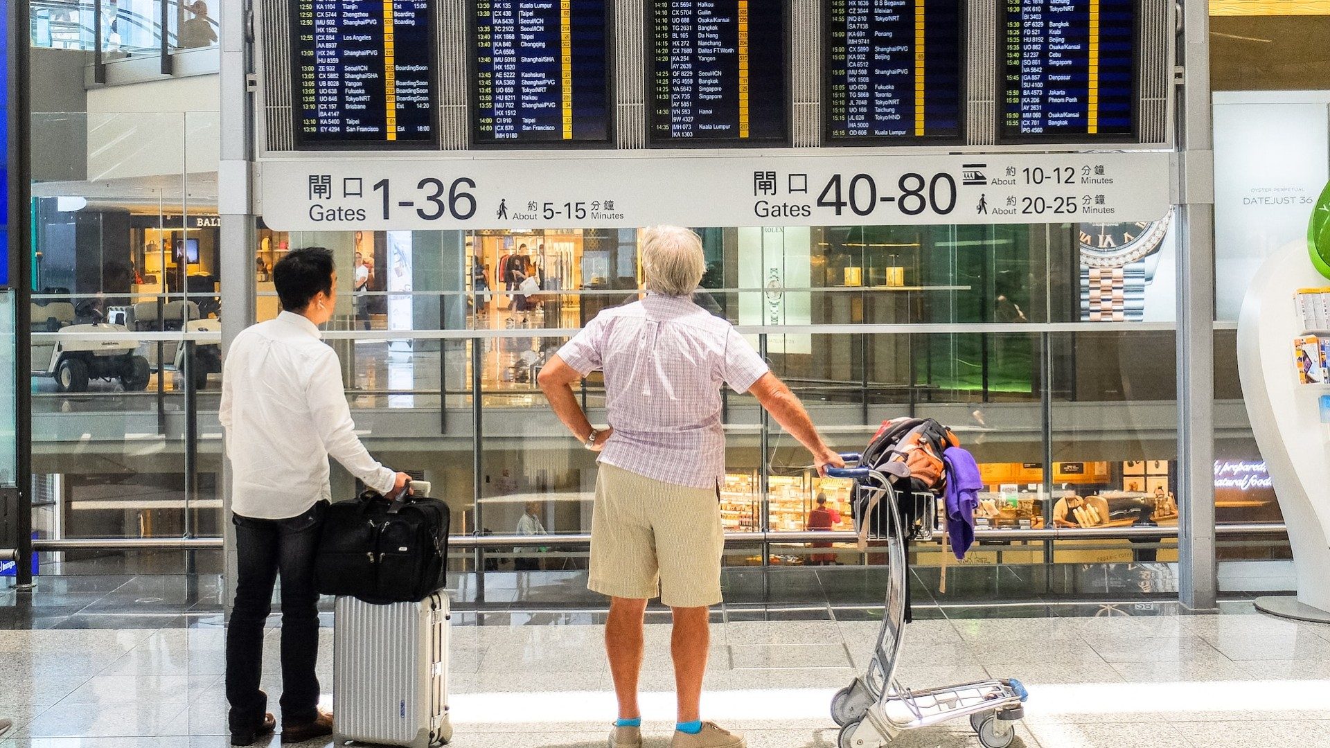 Reisende stehen mit Gepäck am Flughafen und blicken auf die Anzeigetafel