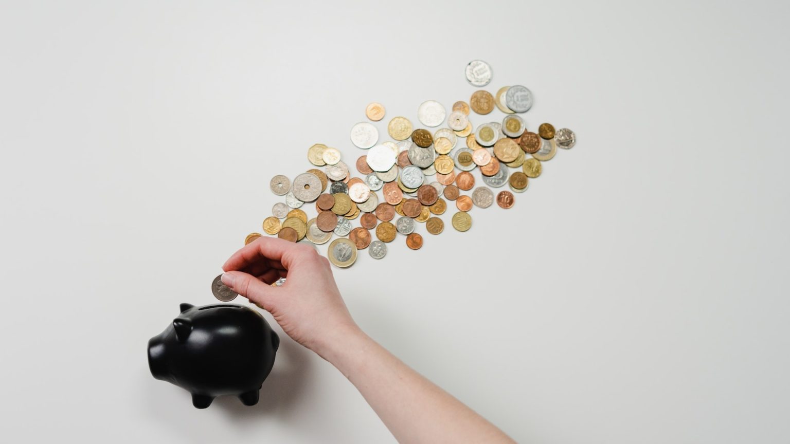 Eine Person steckt eine Münze in ein Sparschwein, neben dem viel Geld liegt. Eine Spardose eignet sich auf für ETFs