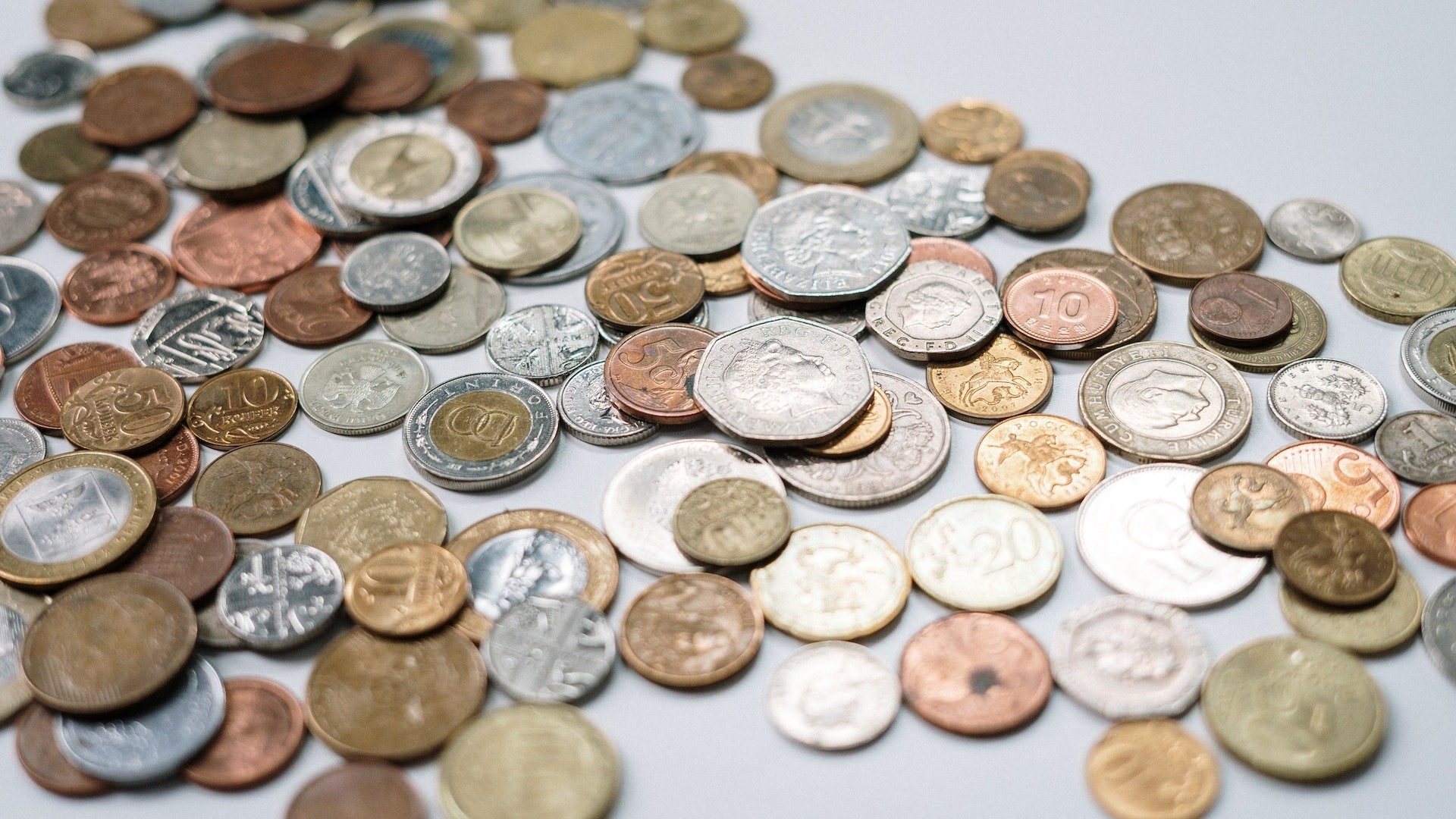 Auf einem Tisch liegen goldene, silberne und bronzene Geldmünzen verschiedener Währungen
