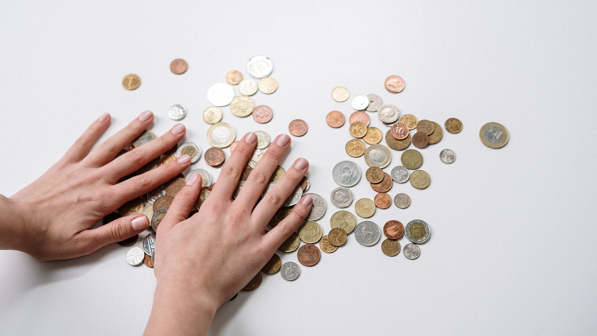 Eine Person nimmt sich Geldmünzen verschiedener Währungen vom einem Tisch