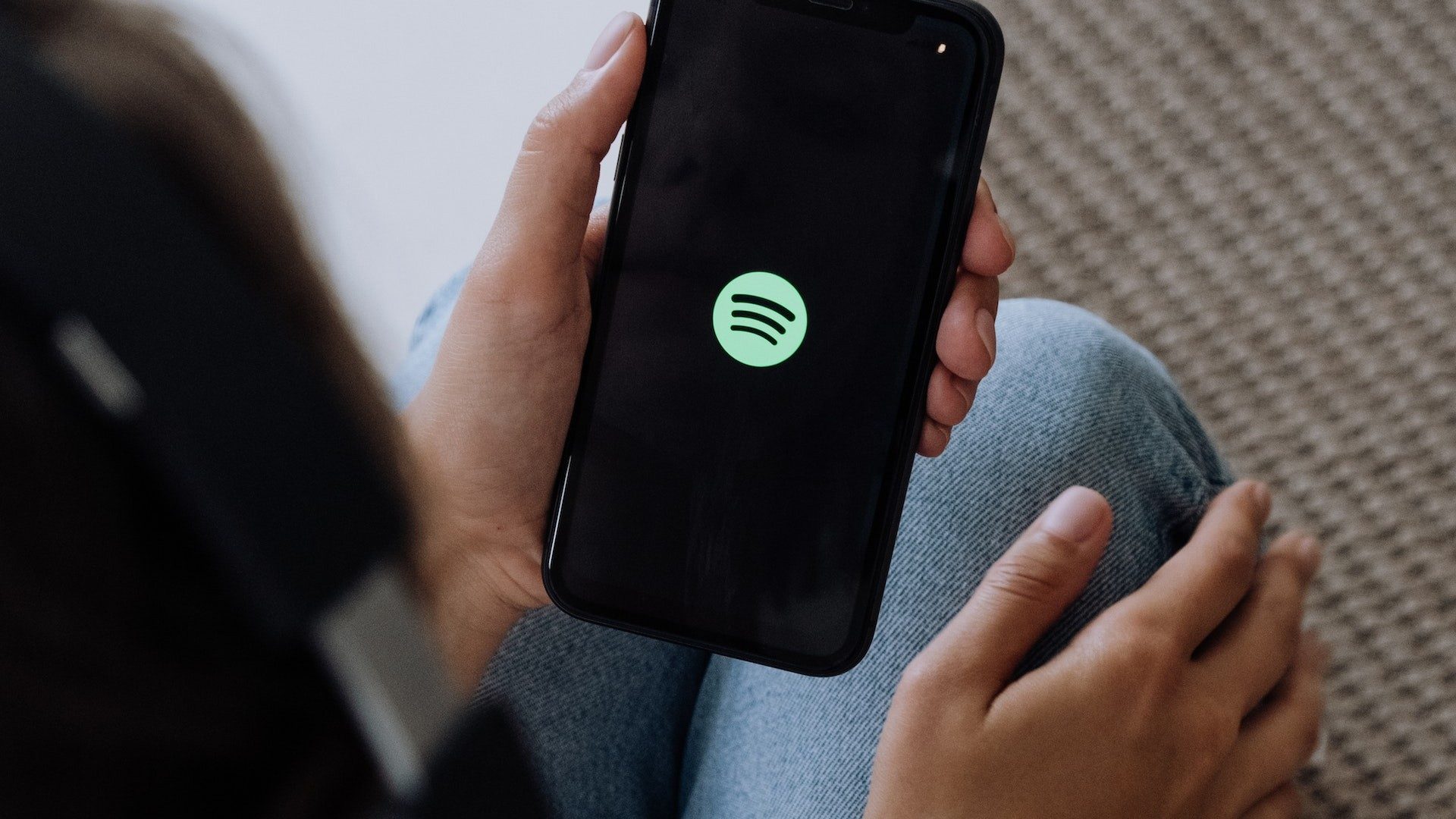 Eine Person mit Kopfhörern startet die App des Musik-Streamingdienstes Spotify