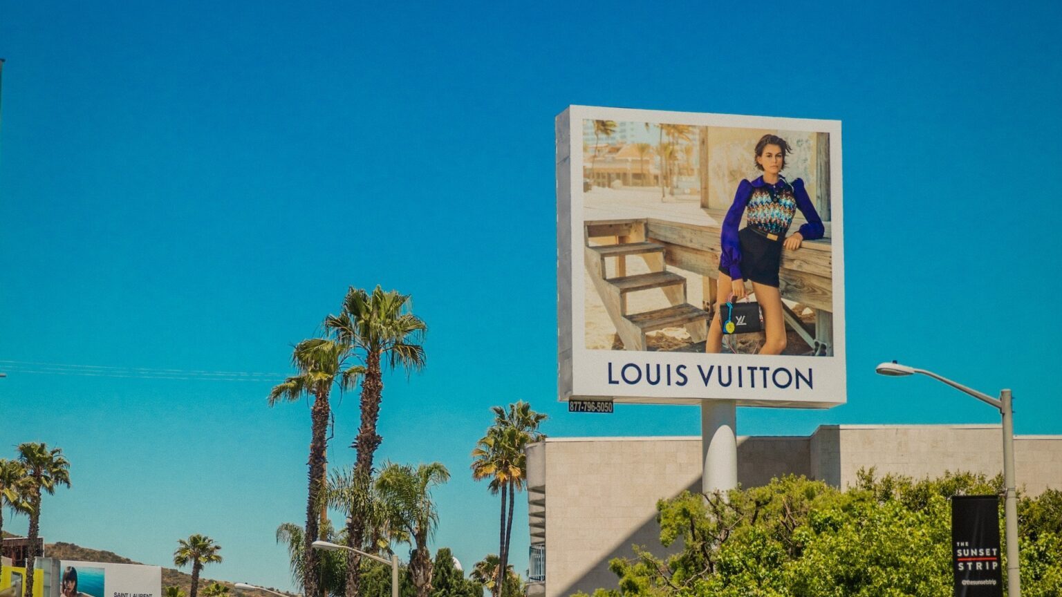 Ein Schild mit der Aufschrift "Louis Vuitton", eine Marke von LVMH, umgeben von Palmen und blauem Himmel