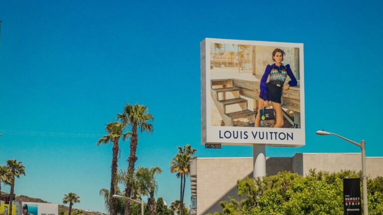 Ein Schild mit der Aufschrift "Louis Vuitton", eine Marke von LVMH, umgeben von Palmen und blauem Himmel