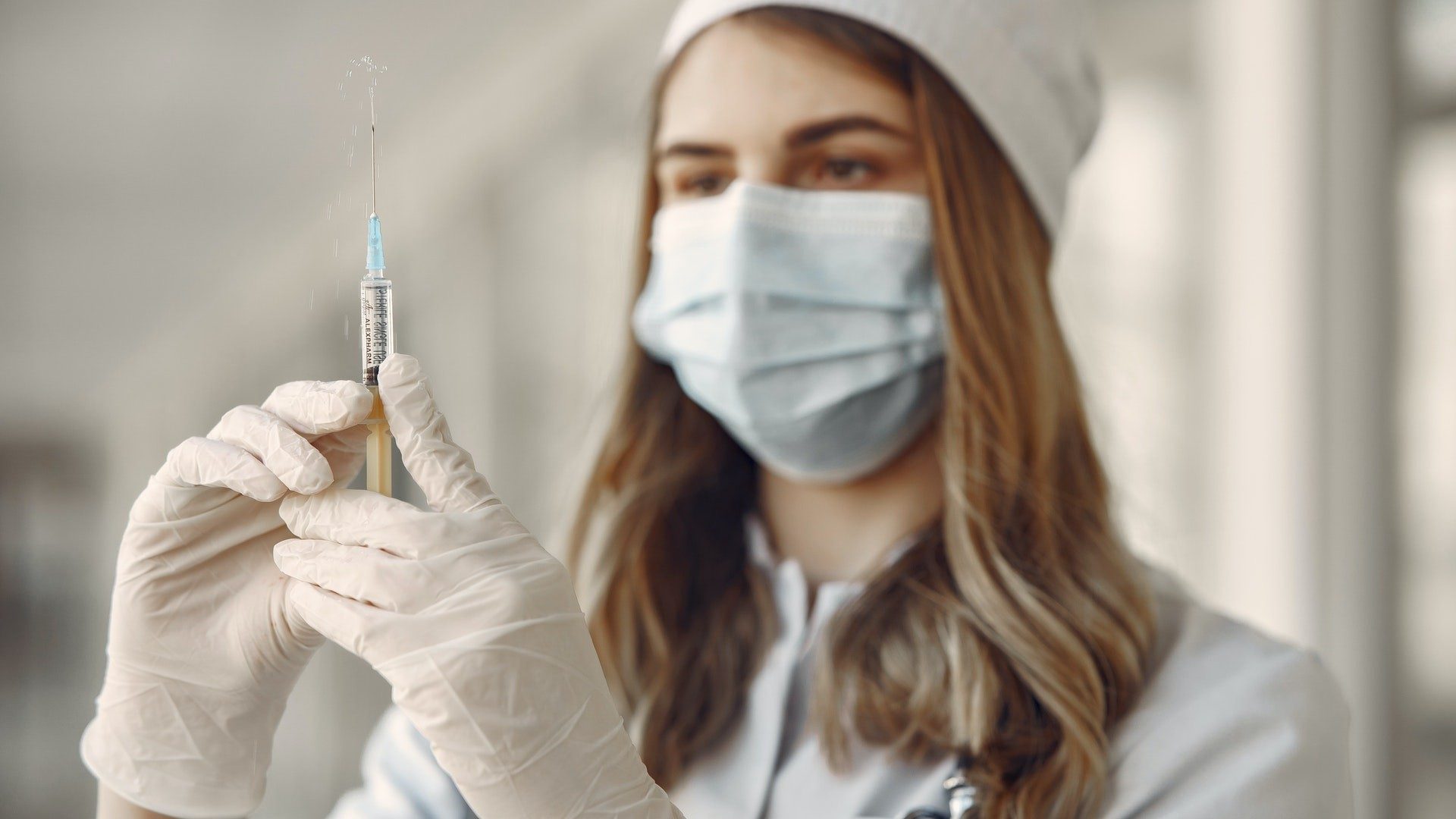 Eine Frau mit Handschuhen und Maske hält eine Spritze mit Medikamenten oder Impfstoff