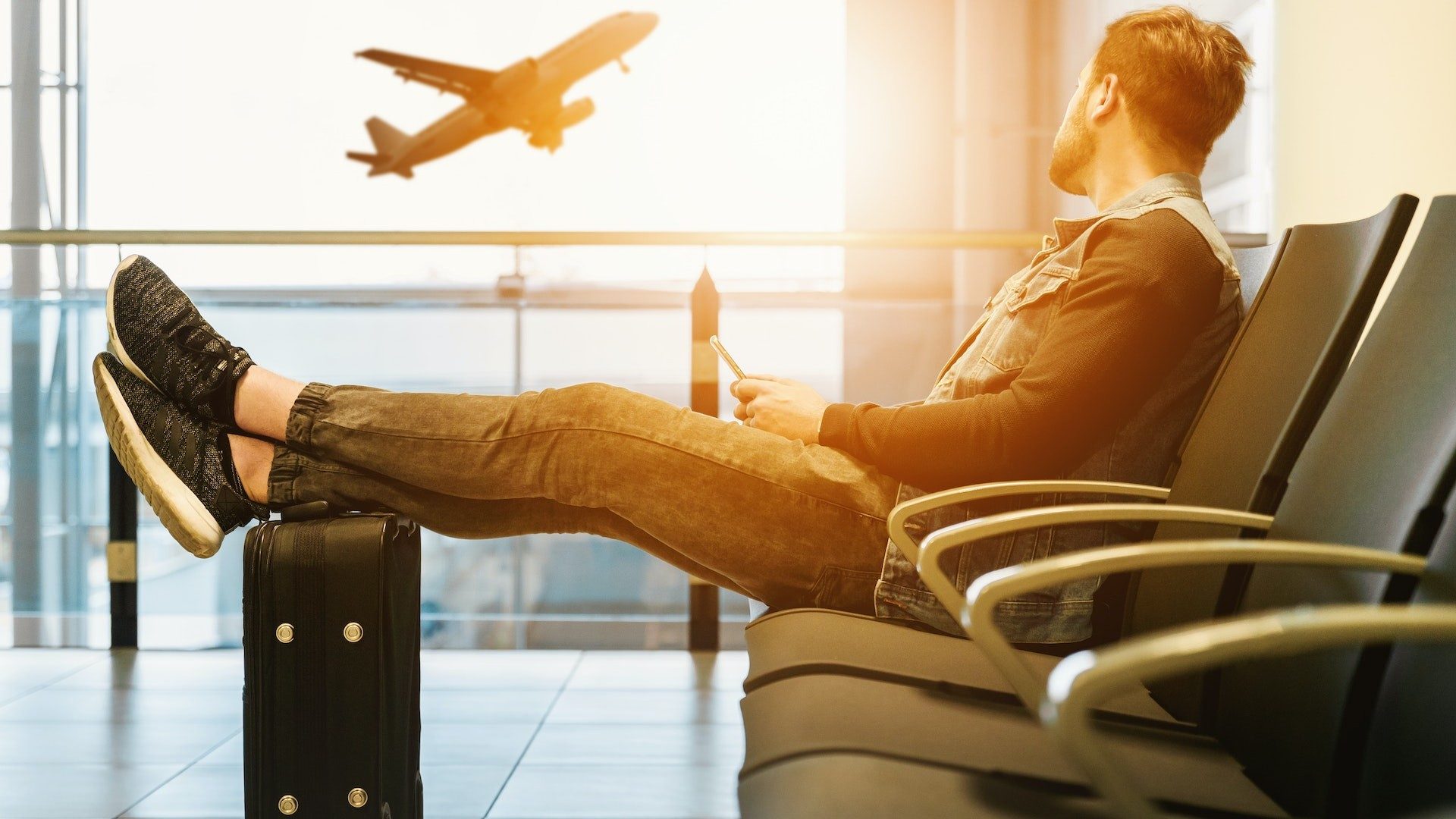 Ein Mann sitzt mit Koffer im Flughafen und wartet auf das Flugzeug für seine Reise