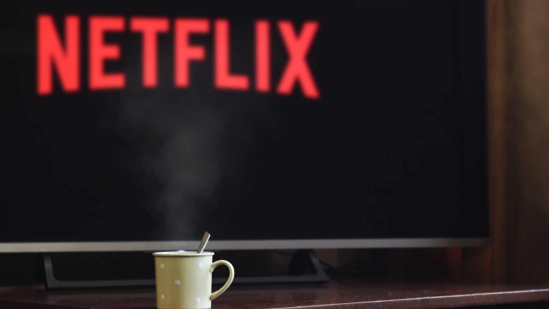 Logo des Streaming-Anbieters Netflix auf einem Fernseher, im Vordergrund eine Tasse