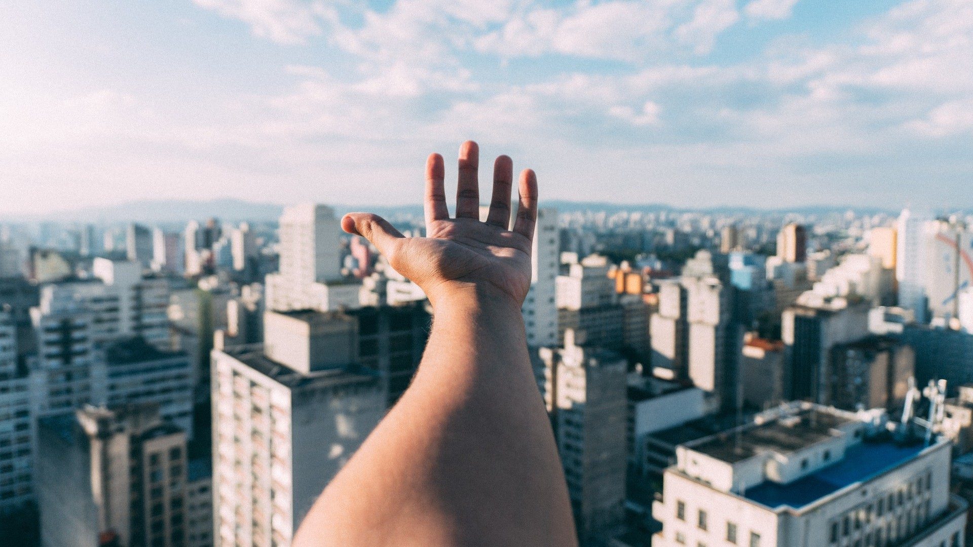 Eine Person streckt ihre Hand vor der Skyline einer Stadt mit zahlreichen Hochhäusern aus