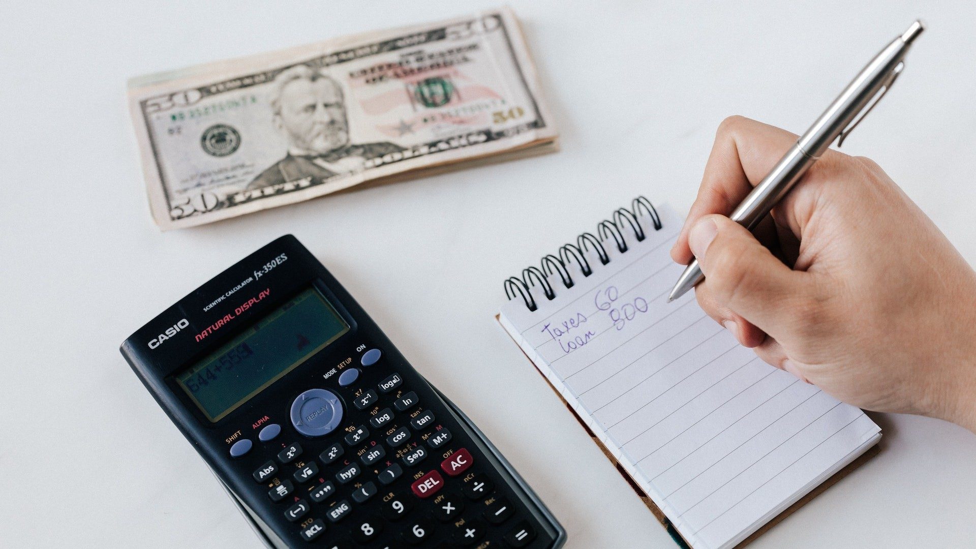Eine Person mit Stift, Papier, Taschenrechner und Geldscheinen plant ihre Finanzen