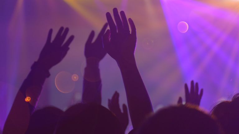 Hoch die Hände: Menschen feiern auf einem Konzert mit Lichtshow