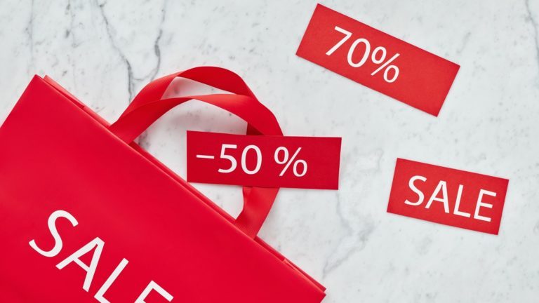 Eine rote Einkaufstüte und weitere Papierschnipsel weisen auf Sale und starke Rabatte im Handel hin