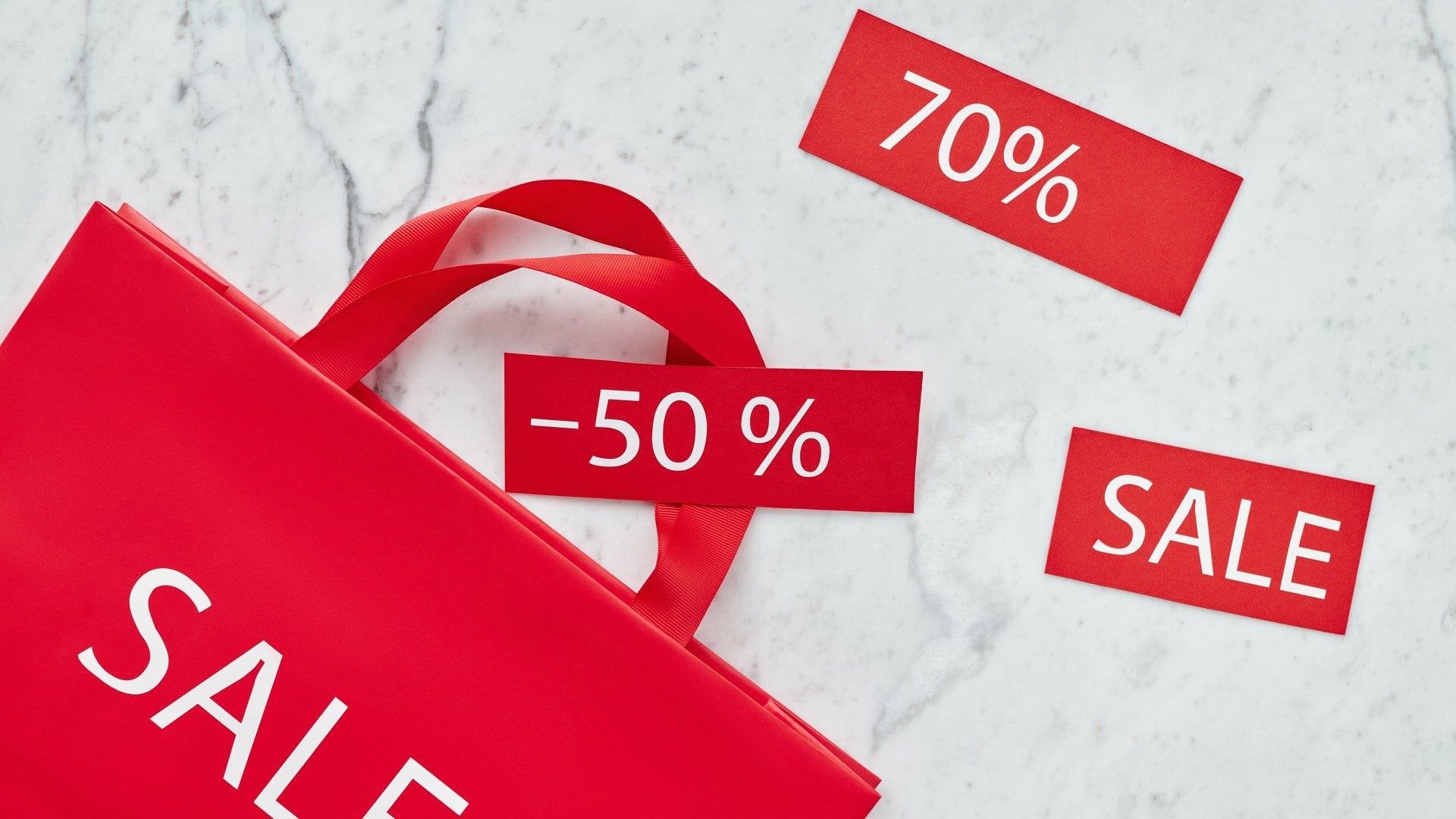 Eine rote Einkaufstüte und weitere Papierschnipsel weisen auf Sale und starke Rabatte im Handel hin