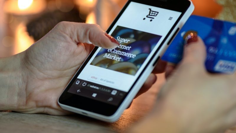 Eine Person mit Smartphone und Kreditkarte kauft Online bei E-Commerce-Anbietern ein