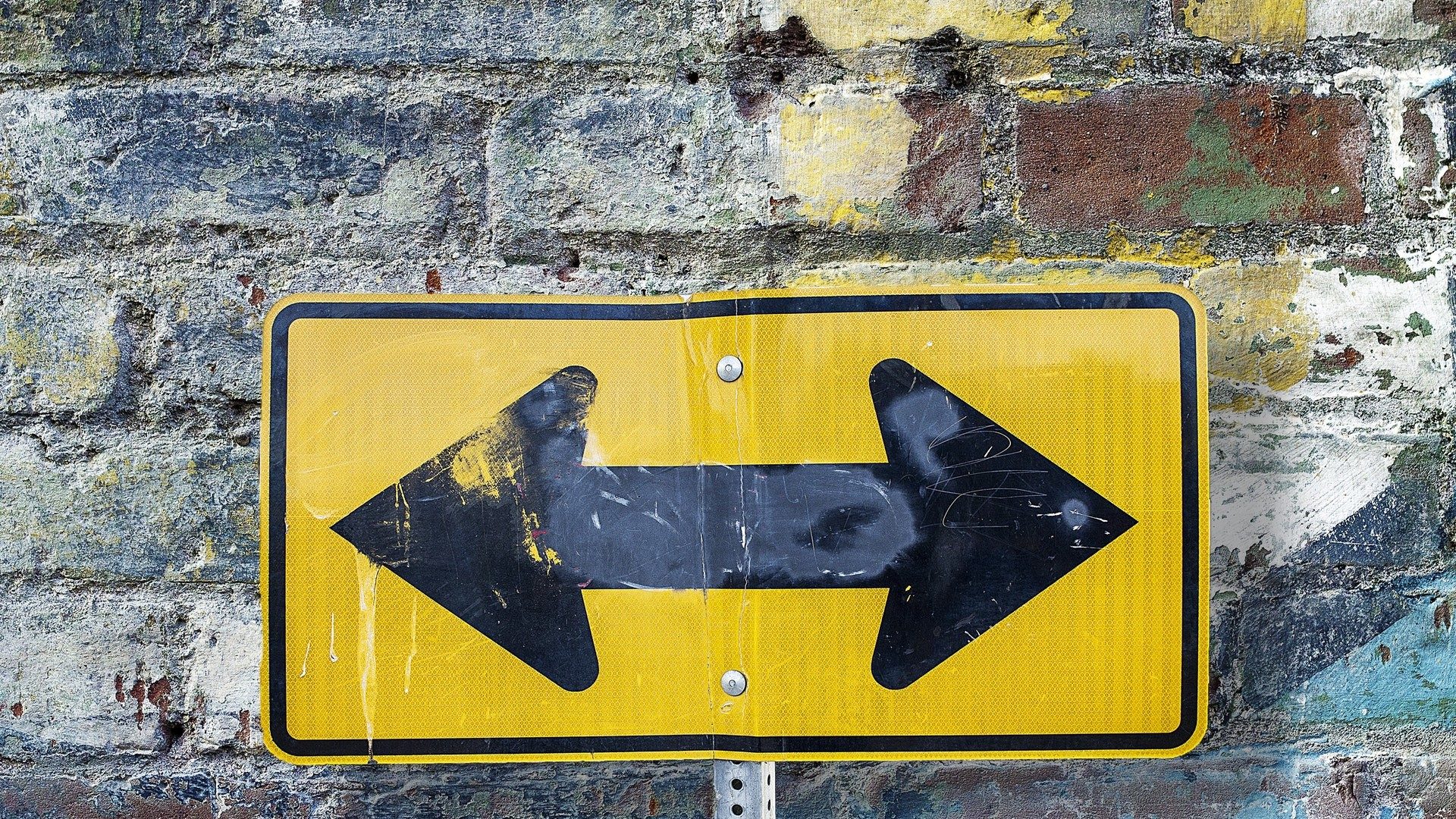 Das Bild zeigt ein Verkehrsschild mit beiden Richtungen vor einer Backsteinmauer.