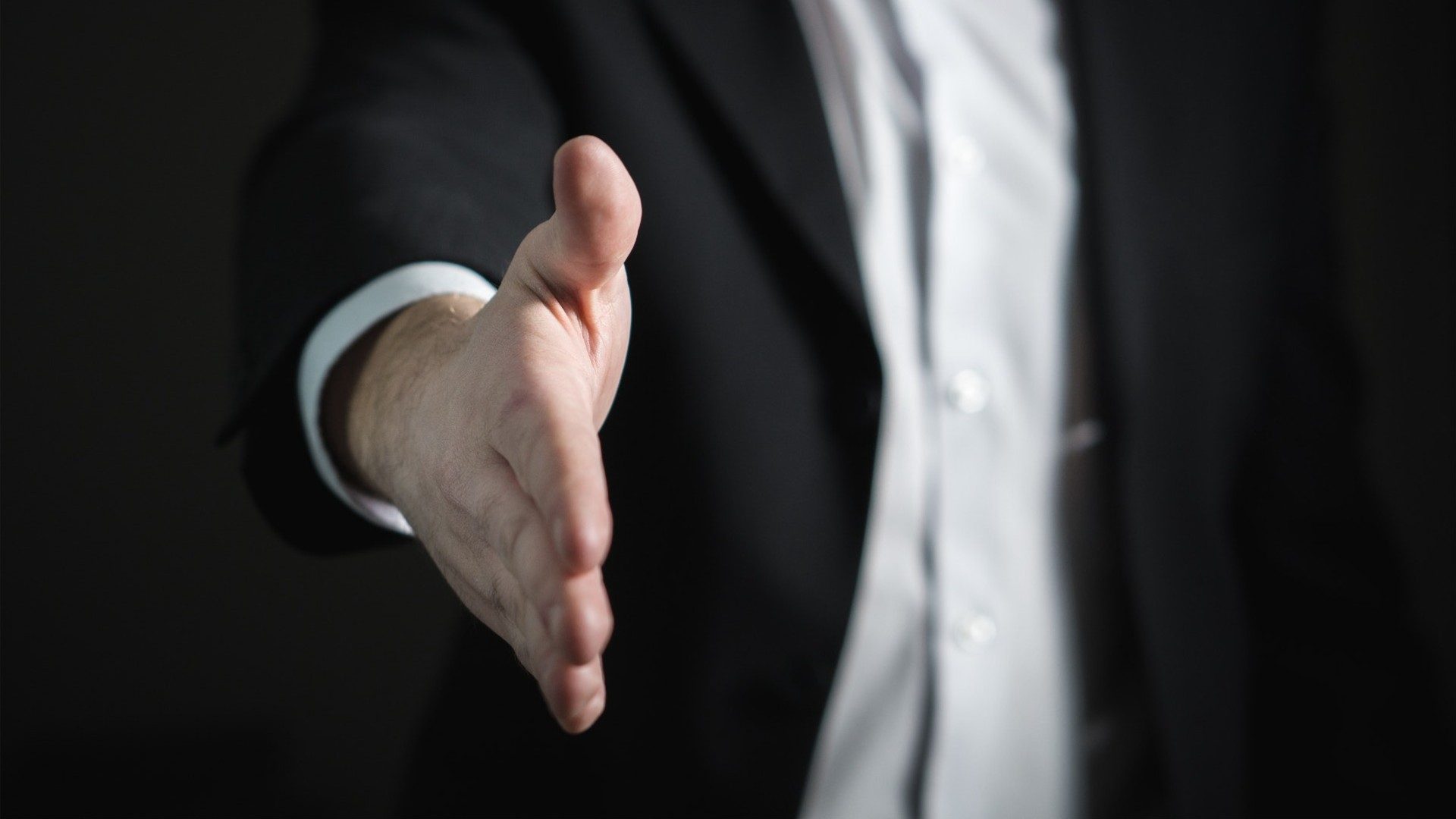 Ein Geschäftsmann im Anzug reicht die rechte Hand zur Begrüßung oder zum Deal