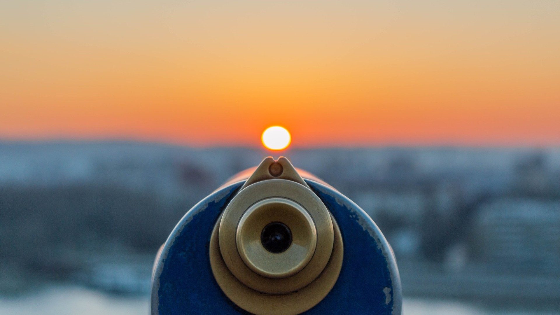 Das Bild zeigt ein Fernrohr durch den man den Sonnenuntergang im Hintergrund beobachten kann.