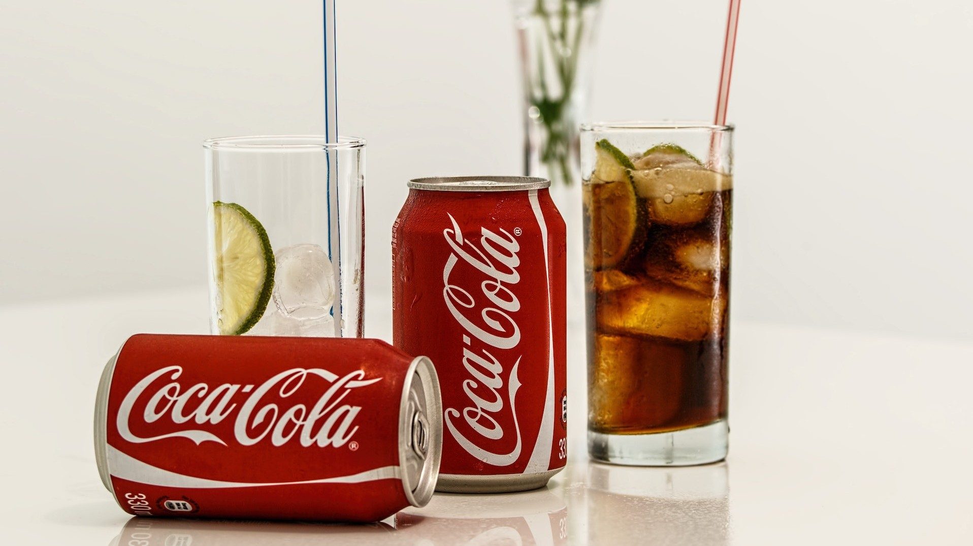 Zwei Getränkedosen von Coca-Cola und zwei Limonadengläser auf einem Tisch