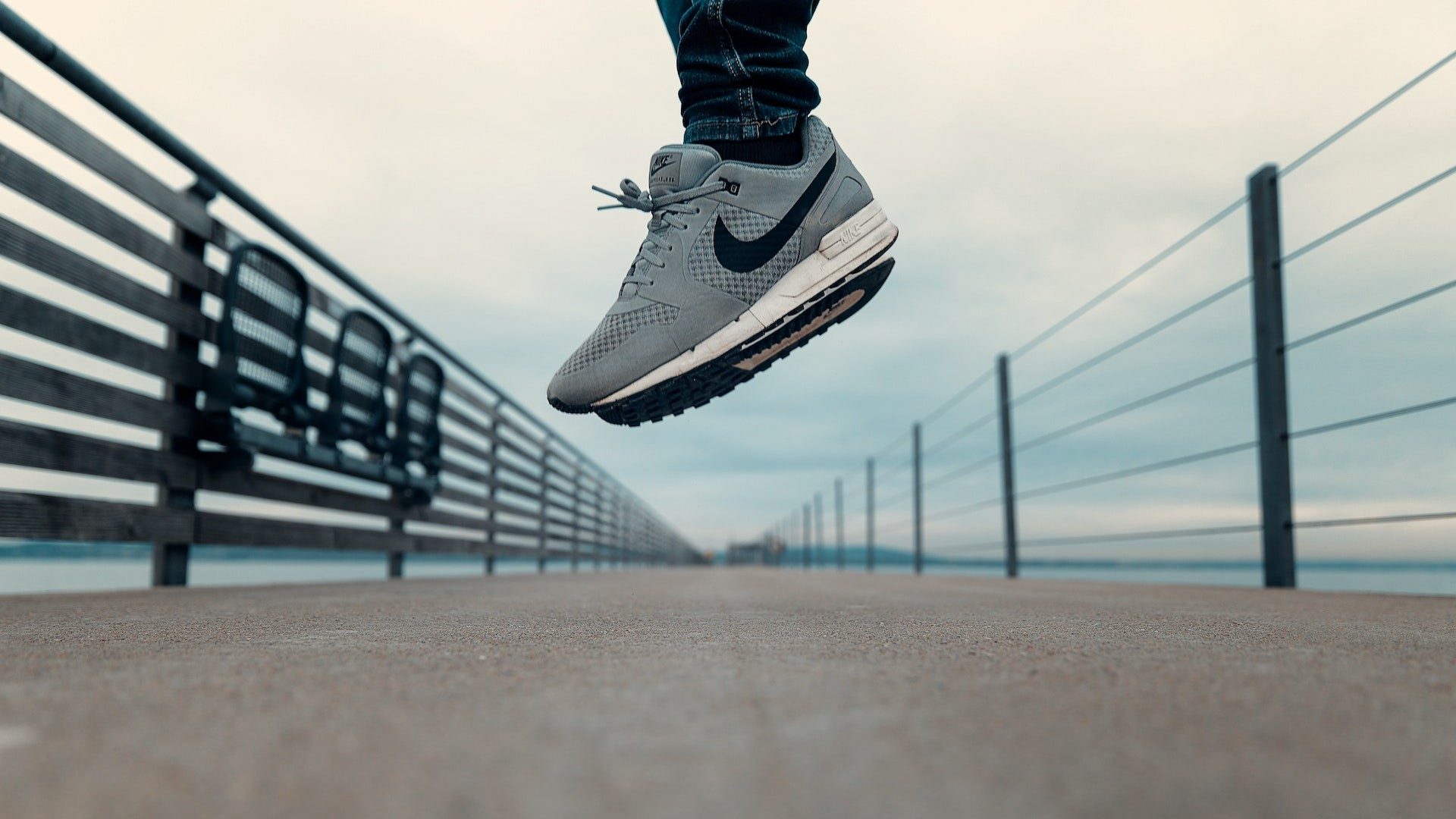 Eine Person mit grauen Nike-Sportschuhen hüpft auf einer Brücke
