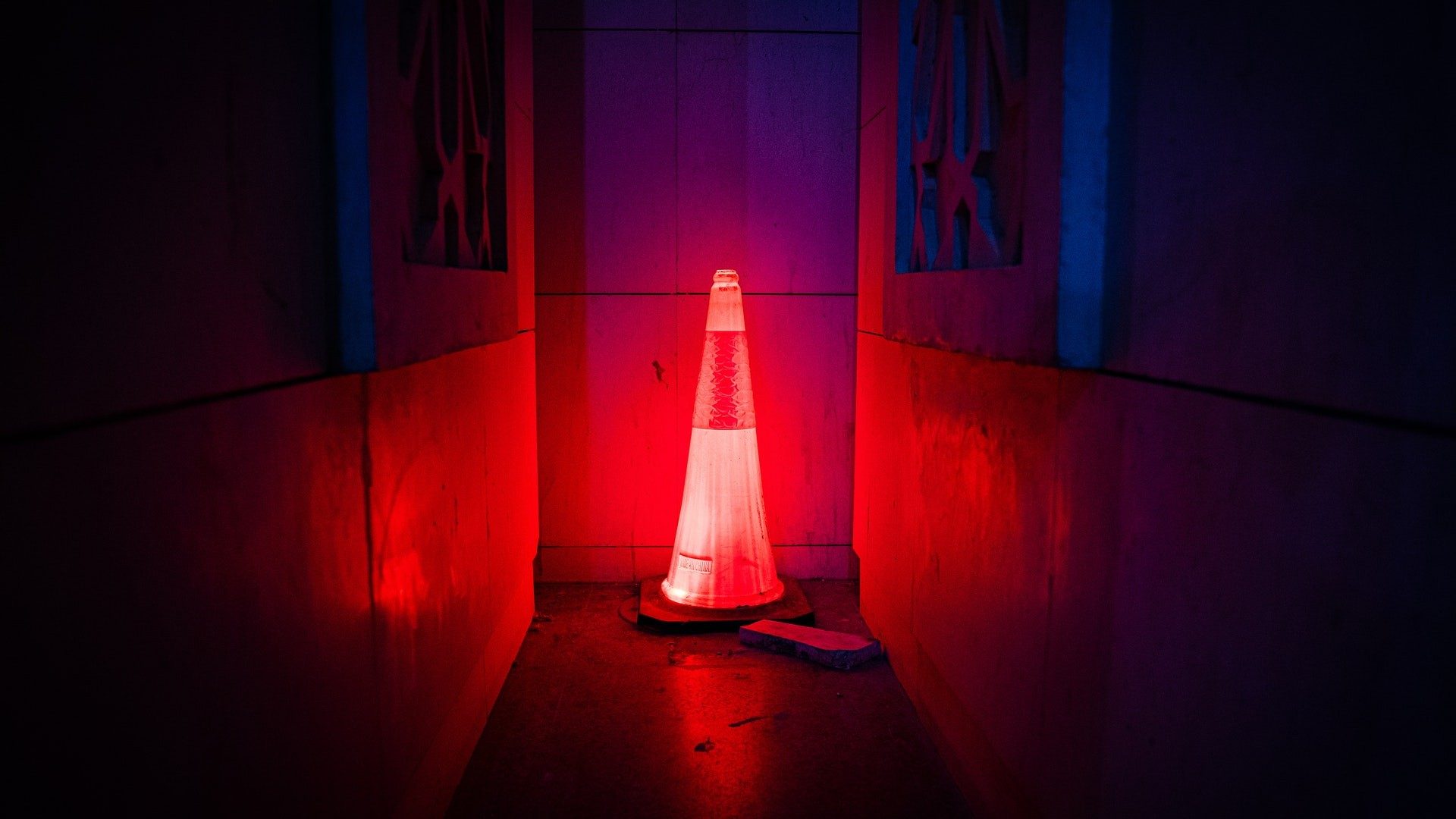 In einem Flur steht ein Kegel der rot leuchtet. Über dem Kegel hängen Bilder.