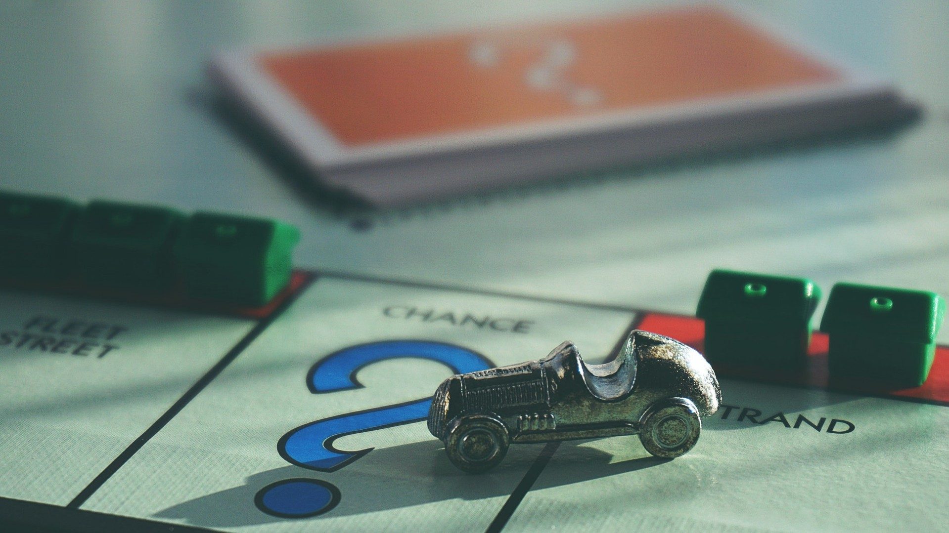 Ein Monopoly-Spiel mit einem Rennauto als Spielfigur und Häusern im Hintergrund.