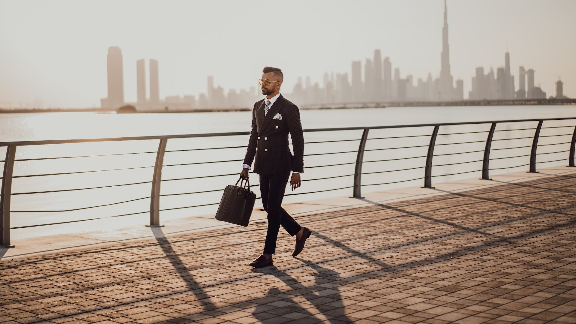 Ein Geschäftsmann im Anzug läuft mit einer Aktentasche eine Promenade entlang, im Hintergrund die Skyline von Dubai