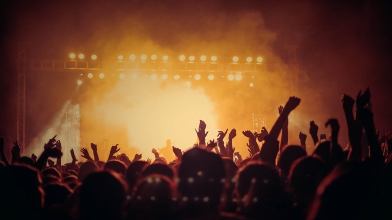 Die Gäste bei einer Konzert-Show jubeln und feiern; im Hintergrund die beleuchtete Bühne