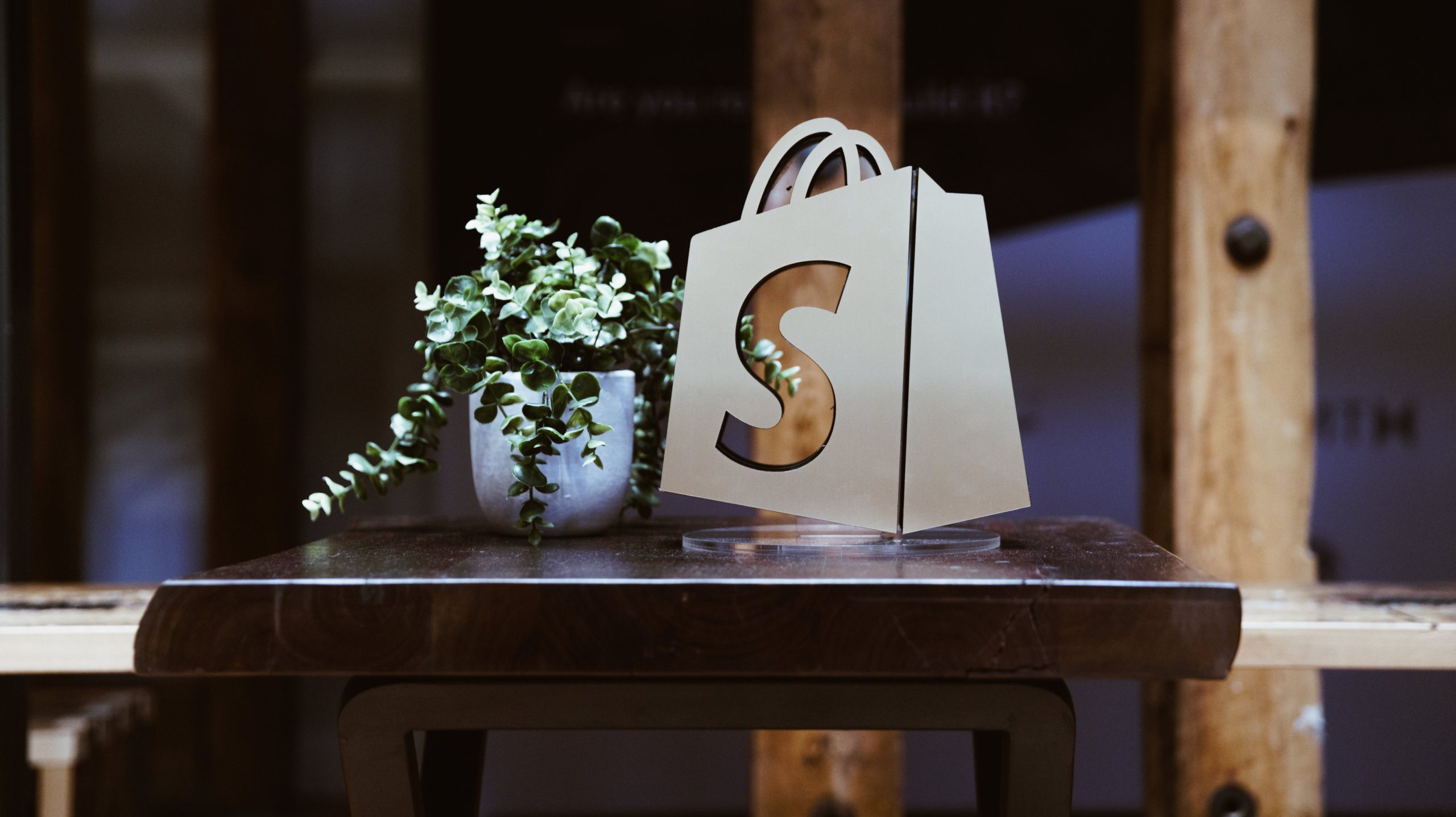Darstellung des Shopify-Logos neben einer Pflanze auf einem Tisch