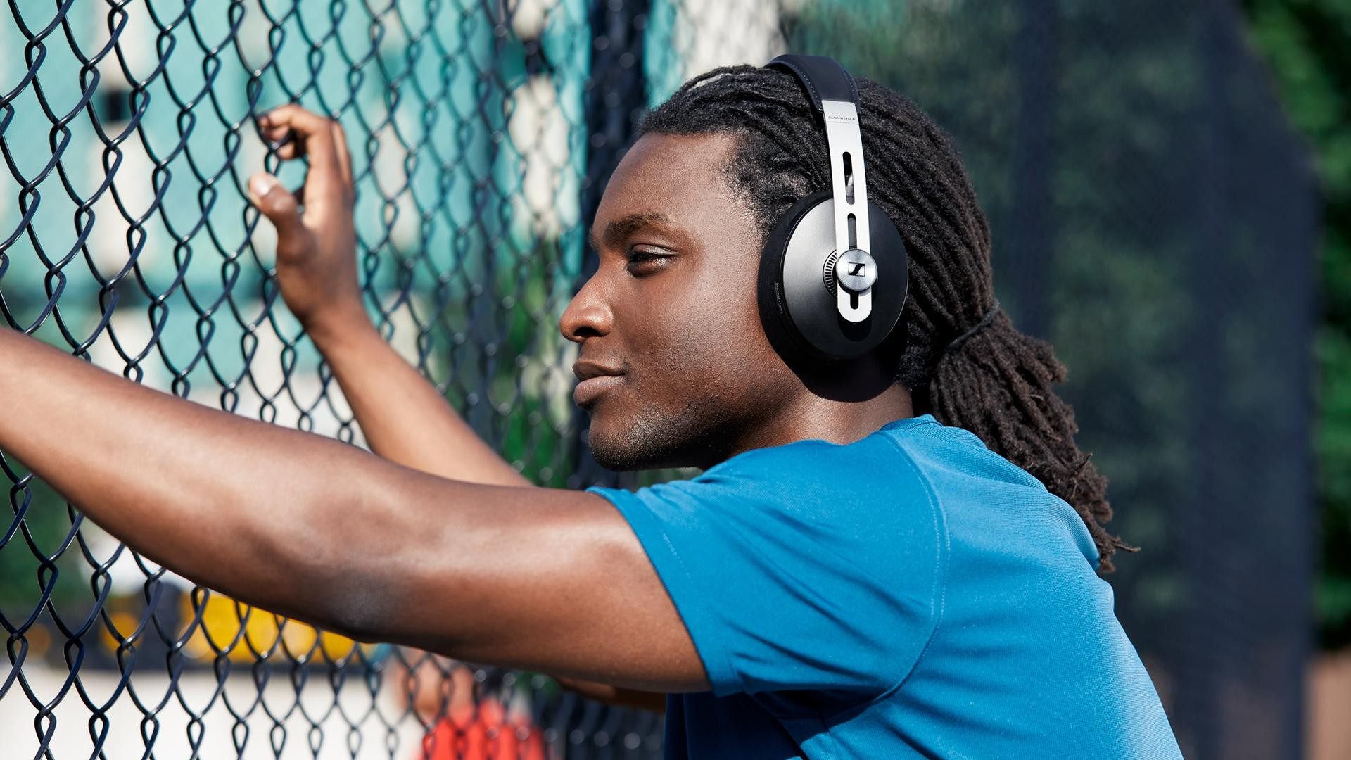 Ein junger Mann hört Musik über einen Kopfhörer und hält sich an einem Gitter fest.
