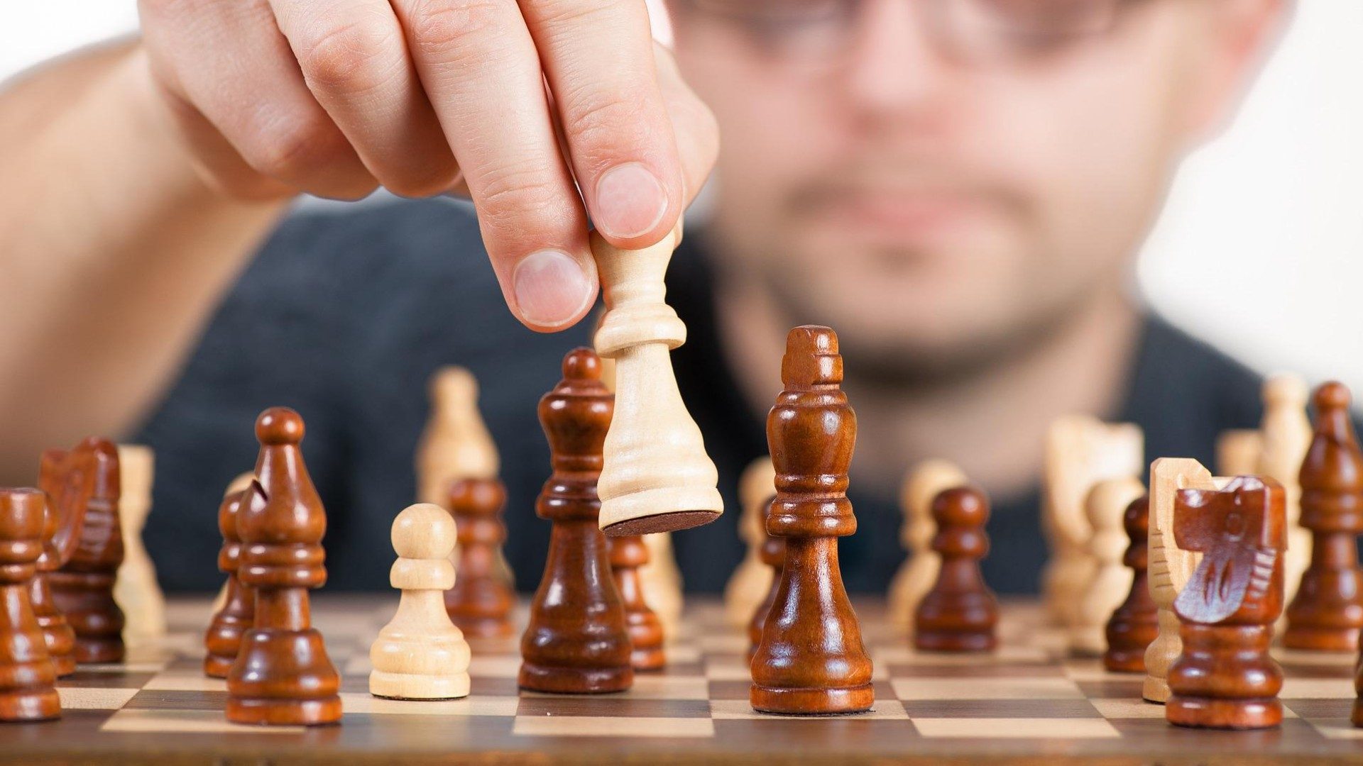 Ein Mann spielt Schach und zieht gerade eine weiße Figur.