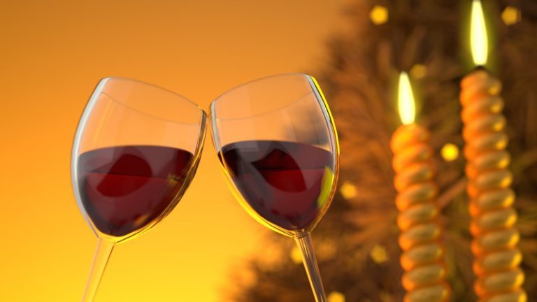 Zwei Gläser Wein umgeben von festlicher Dekoration und Beleuchtung.