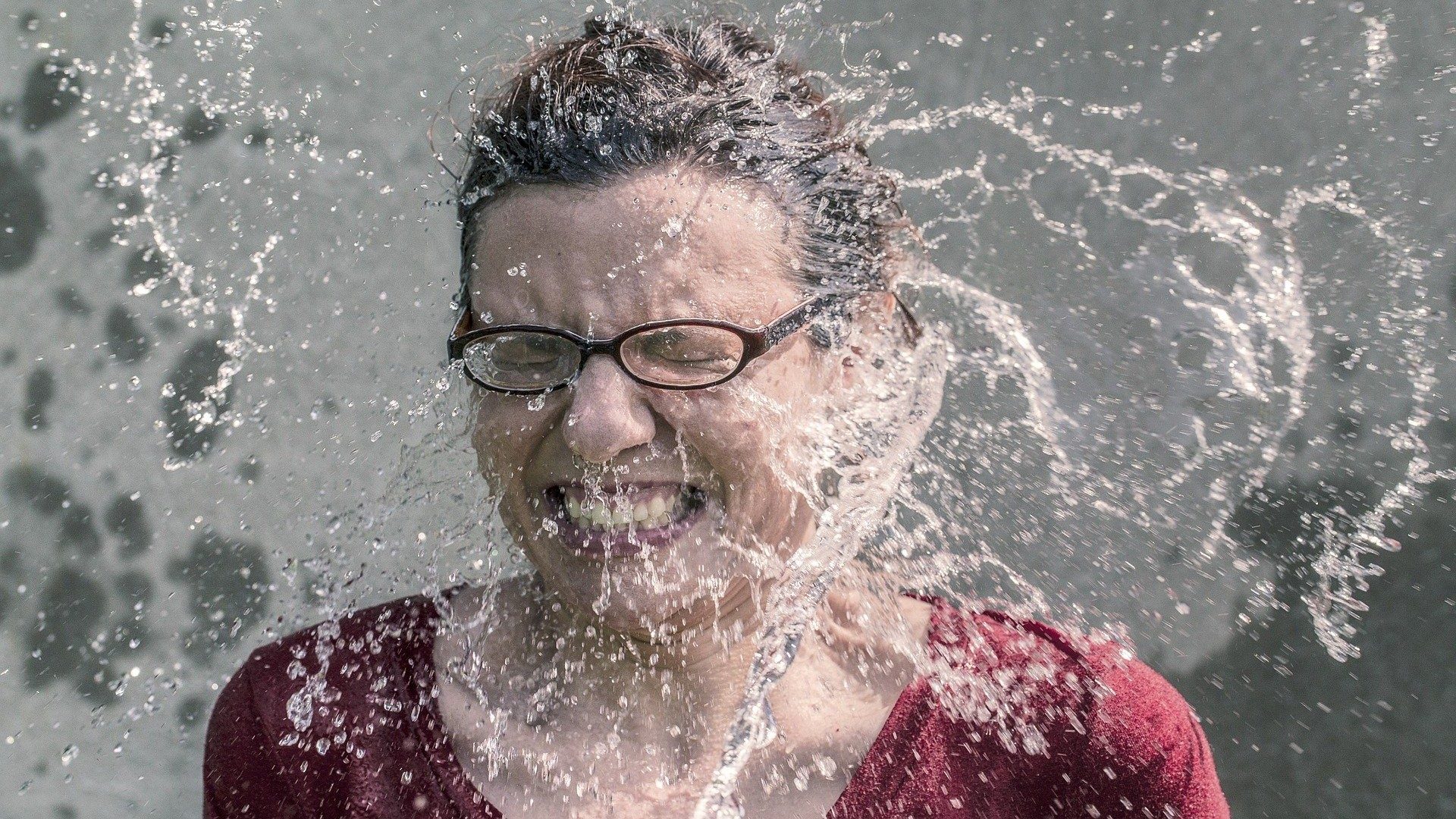 Einer Frau mit Brille spritzt Wasser ins Gesicht.