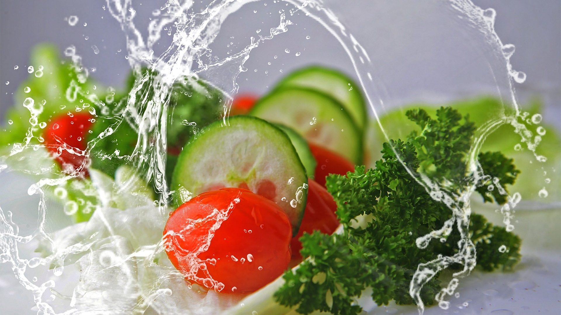 Wasser schwappt über einen frischen Salat mit Tomaten, Gurken und Petersilie